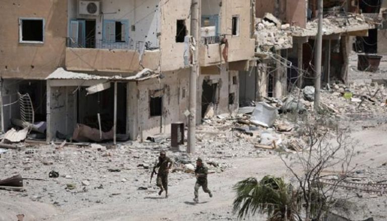 مقاتلان من قوات سوريا الديمقراطية يركضان وسط منازل مهدمة في الرقة