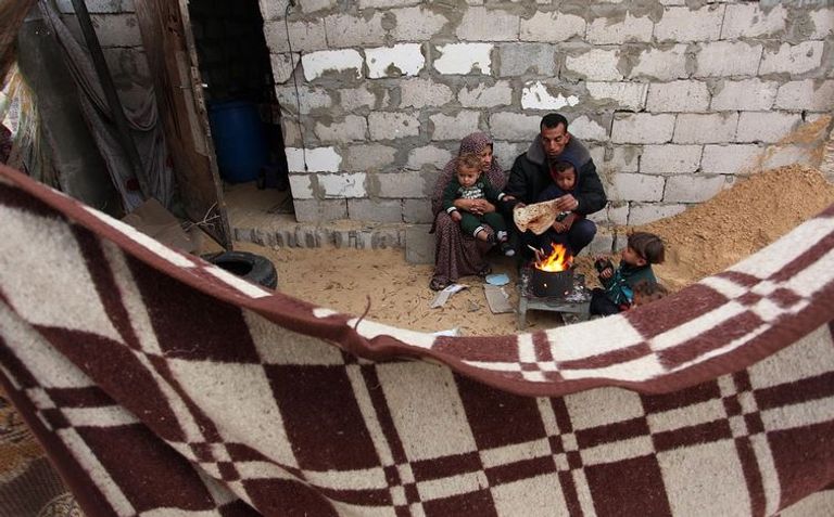 أسرة فلسطينية تلتمس الدفء خلال موجة البرد القارس في القطاع سيدة فلسطينية تحتمي من الأمطار وبرودة الطقس في قطاع غزة