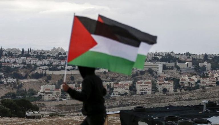 شاب فلسطيني يرفع علم بلاده أمام المستوطنات الإسرائيلية