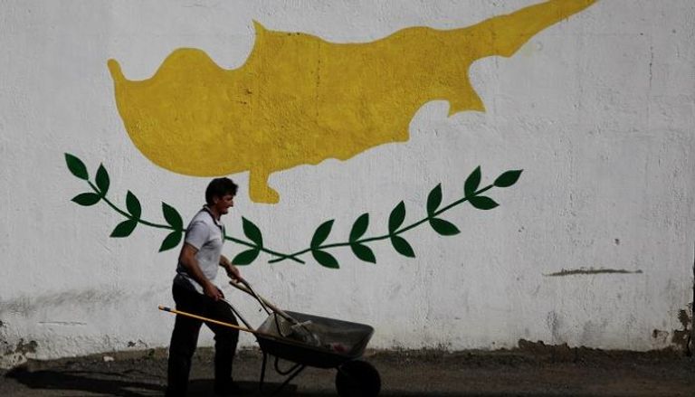 رجل يدفع عربة يد أمام جدار رسم عليه علم قبرص