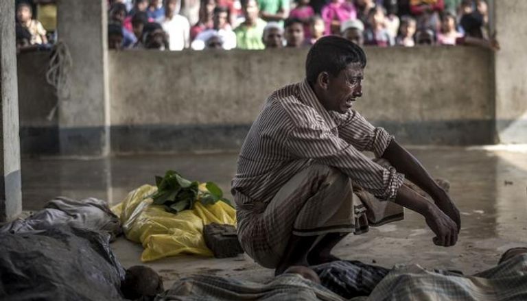 مواطن من الروهينجا يبكي إلى جانب جثث ذويه