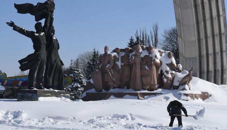 عامل يزيل الثلج من أمام نصب يشير إلى العهد السوفياتي في كييف