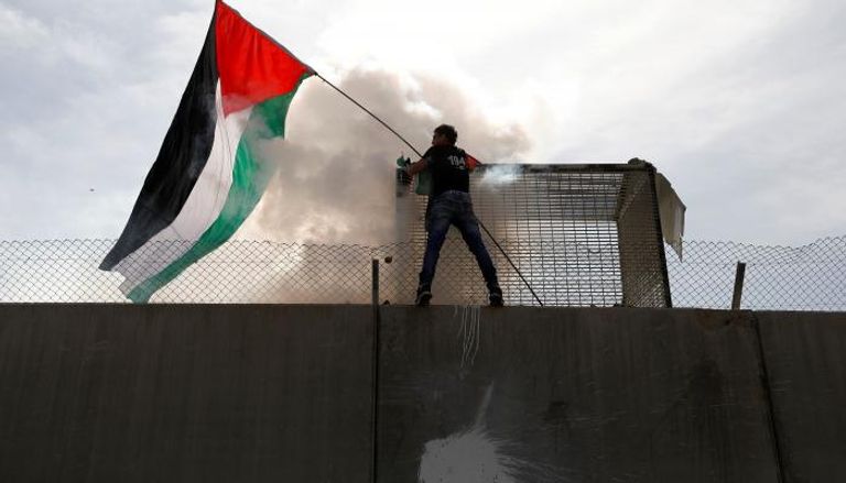 أحد الشبان رافعا علم فلسطين على جدار الفصل الحدودي بغزة - رويترز