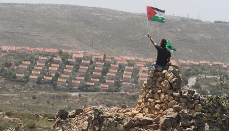 فلسطيني يلوح بعلم بلاده في الضفة الغربية