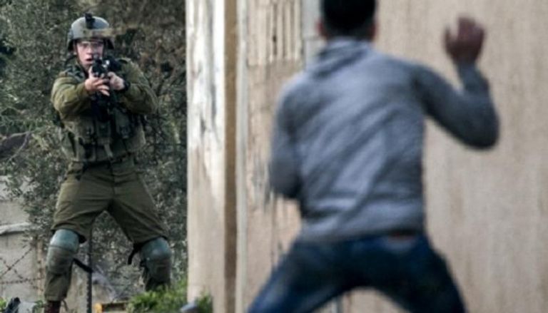 جندي إسرائيلي يصوب سلاحه نحو شاب فلسطيني