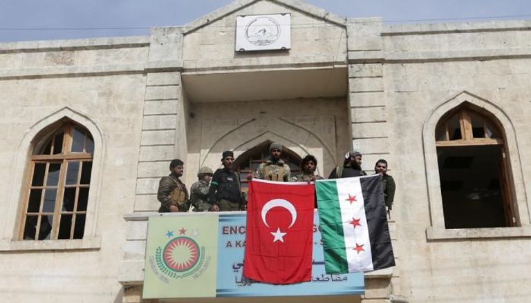 عناصر من الفصائل المسلحة ترفع العلم التركي فوق عفرين تقرير يكشف عن سبل حشد أردوغان التنظيمات لاحتلال المدن السورية