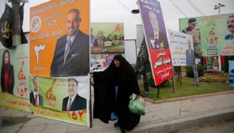 سيدة عراقية تمر إلى جوار لافتات دعائية لمرشحي الانتخابات البرلمانية