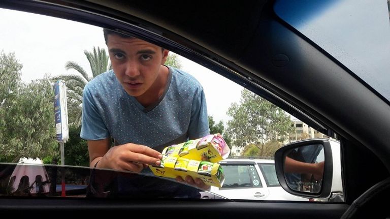 الطفل يوسف أثناء عرض البضائع على قائدي السيارات في إشارات غزة الطفل يوسف خلال بيع إحدى البضائع في إشارات غزة