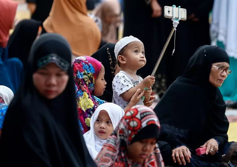 صورة لطفل صغير ممسكًا بعصا "السيلفي" قبل صلاة العيد مهرج يوزع بالونات على الأطفال قرب مصلى مسجد قبة الصخرة