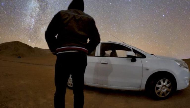 ظل الراصد يظهر على سيارته وفي الخلفية نجوم درب التبانة 