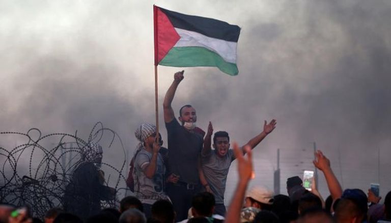 شبان فلسطينيون يحملون العلم قرب السياج الحدوي - رويترز