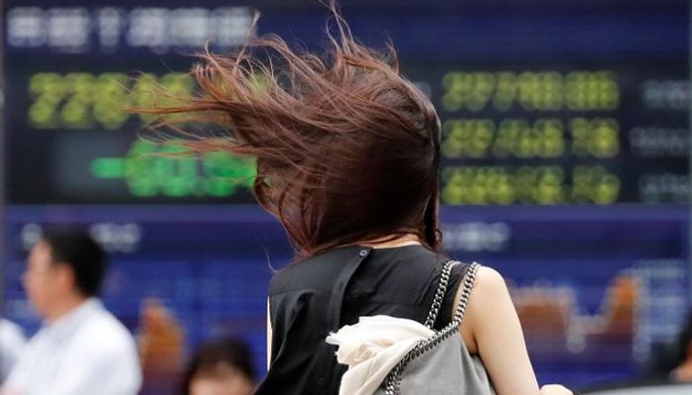 امرأة تسير أمام لوحة أسعار الأسهم الإلكترونية في طوكيو