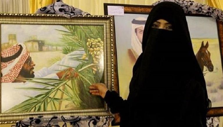 التشكيلية الإماراتية هدى الريامي أمام إحدى لوحاتها