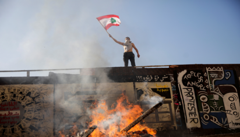 متظاهر يحمل علما فوق سور بأحد شوارع لبنان