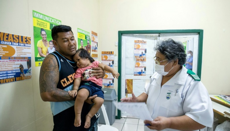 رجل يحمل ابنته في عيادة بمدينة أبيا في ساموا التي ينتشر فيها وباء الحصبة