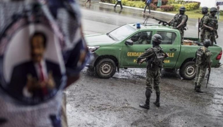 أحد مؤيدي رئيس الكاميرون بول بيا إلى جانب عناصر من قوات الأمن