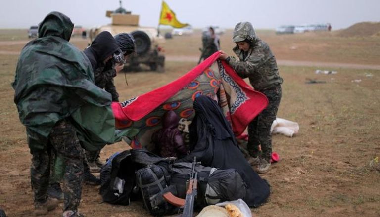 عناصر من قوات سوريا الديمقراطية يساعدون امرأة قرب الباغوز