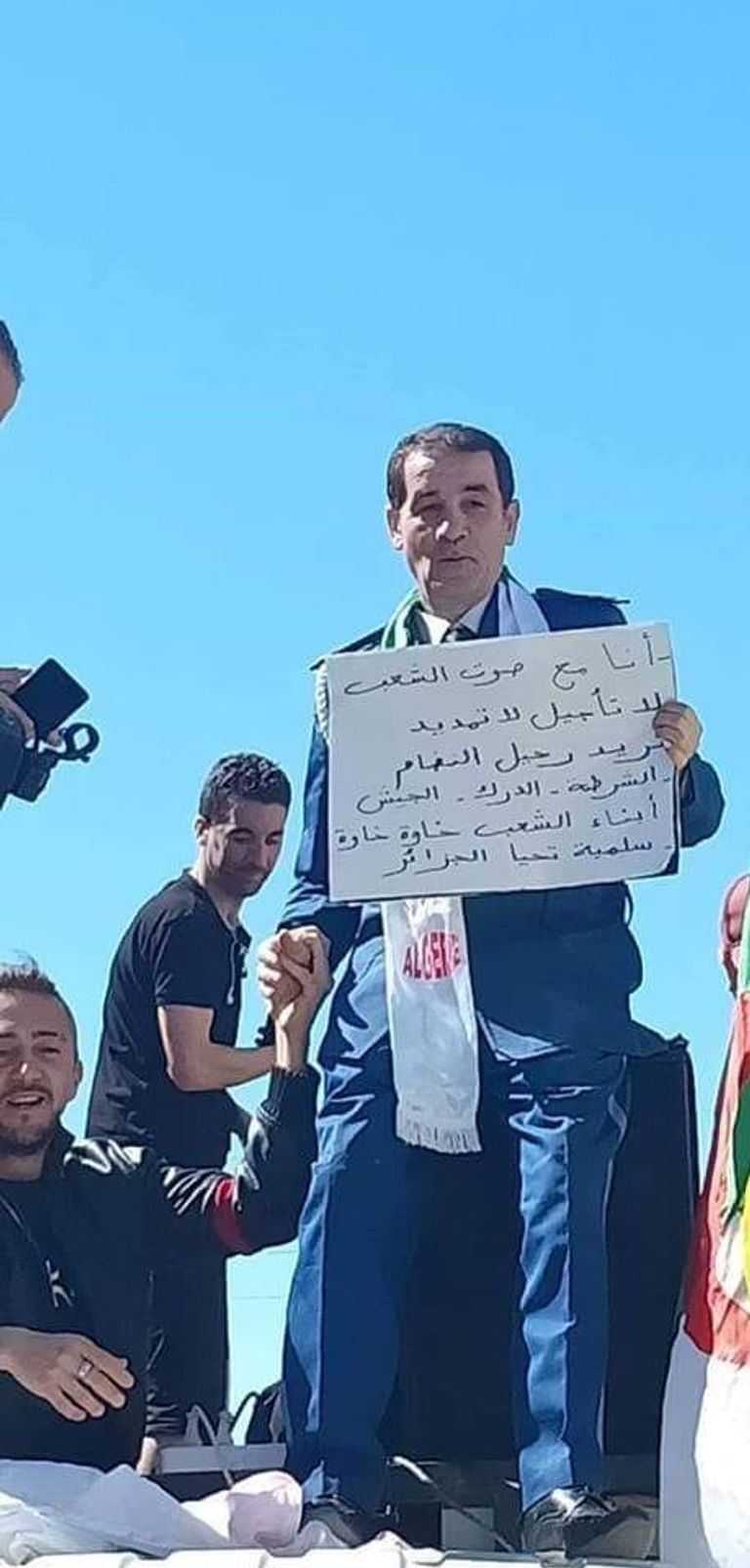 شرطي جزائري ينضم إلى المظاهرات طفل يحمل راية الجزائر على ظهر جده في مظاهرات الجمعة