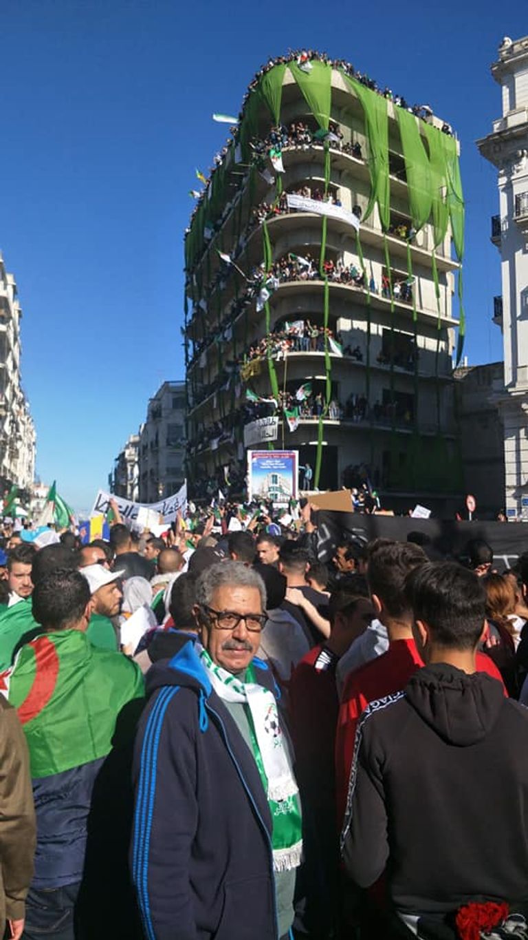 جزائريون في مبنى غير مكتمل طفل يحمل راية الجزائر على ظهر جده في مظاهرات الجمعة