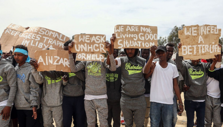 مهاجرون يحملون لافتات أثناء زيارة جوتيريس لطرابلس