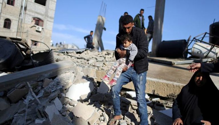 فلسطيني يحمل طفله وسط ركام منزل دمرته إسرائيل في غزة