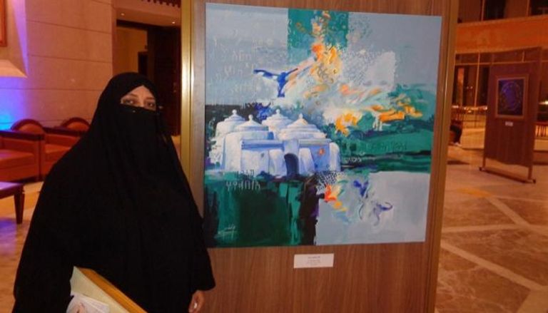 الرسامة الإماراتية منى الخاجة بجانب لوحتها "مسجد البدية"