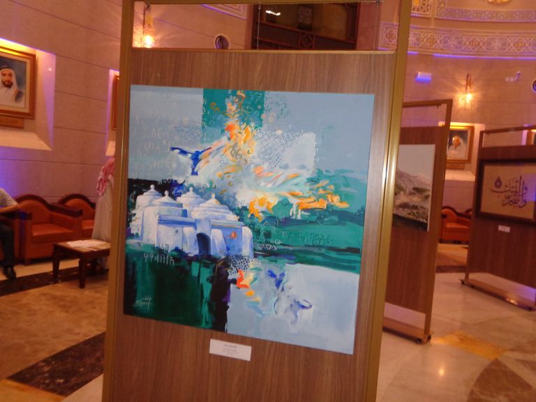 الرسامة الإماراتية منى الخاجة بجانب لوحتها "مسجد البدية"