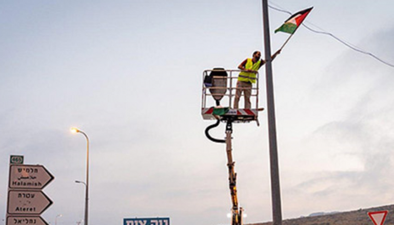 مستوطن يرفع علما فلسطينيا على عامود إنارة