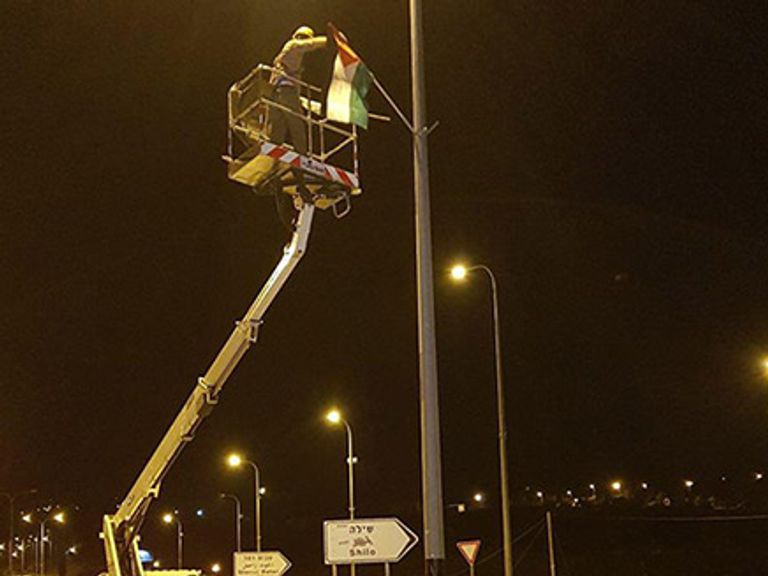 مستوطن يرفع علما فلسطينيا على عامود إنارة