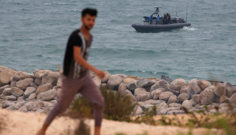فلسطيني يمشي على سواحل غزة ويظهر في الصورة قارب إسرائيلي