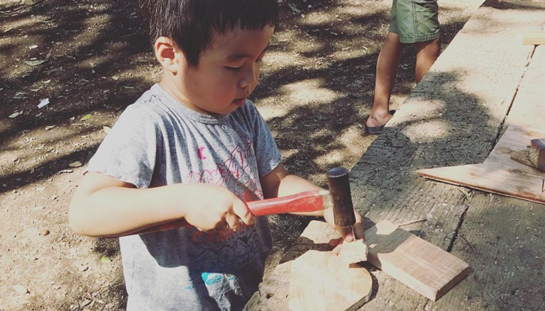 طفل بالحديقة يستخدم مطرقة على لوح خشب