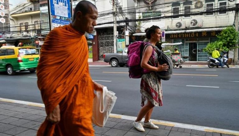 سائحة أرجنتينية تسير بجوار راهب بوذي قرب مطار بانكوك
