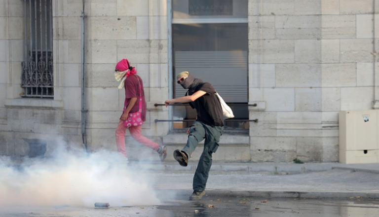 متظاهر يبعد قنبلة غاز عن محيط المظاهرات - الفرنسية