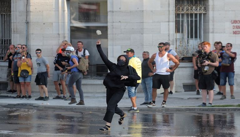 متظاهر يبعد قنبلة غاز عن محيط المظاهرات - الفرنسية