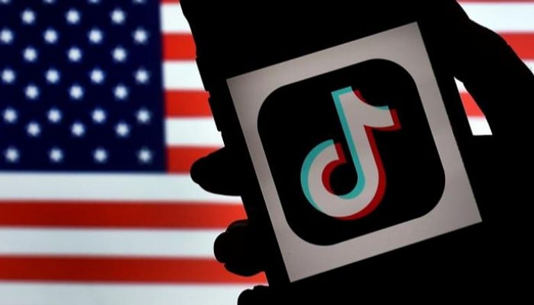 شعار "تيك توك" على شاشة هاتف آيفون خلفه العلم الامريكي – أ ف ب
