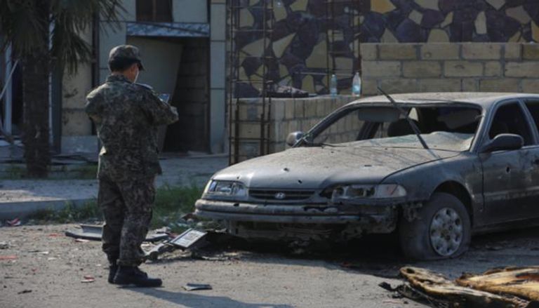 جندي يقف أمام سيارة دمرها القصف في ناغورني قره باغ