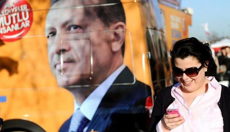 امرأة تركية تنظر إلى هاتفها بجوار لافتة لأردوغان - أ.ف.ب