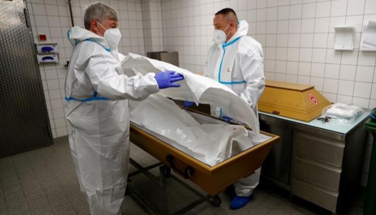 أطباء ألمان يضعون جثة أحد المتوفين بكورونا في تابوت
