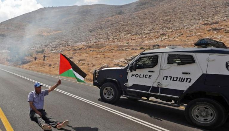 فلسطيني يلوح بعلم بلاده أمام مركبة أمن إسرائيلية