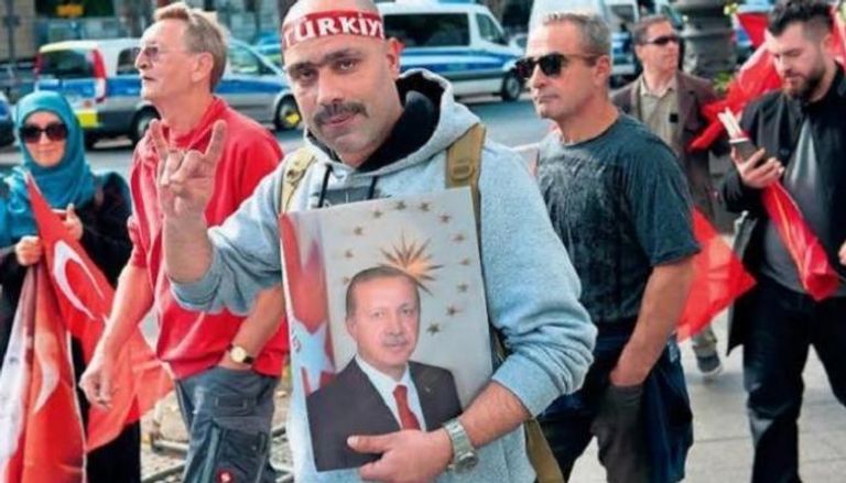 تركي بألمانيا يحمل صورة أردوغان ويشير بشعار الذئاب الرمادية