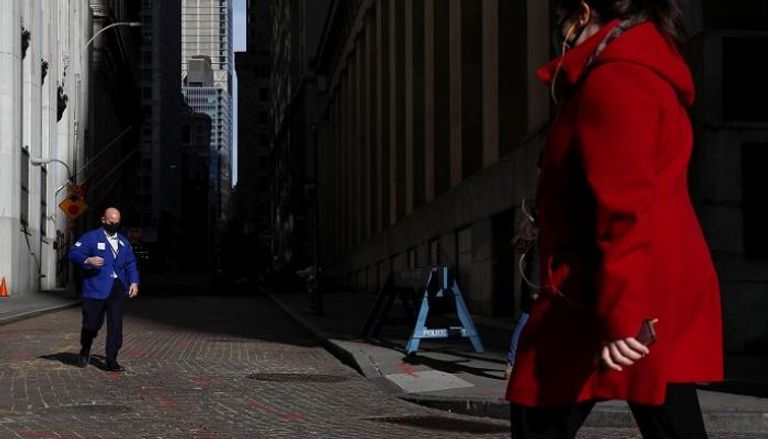 متداول يرتدي قناعًا يسير خارج بورصة نيويورك - رويترز 