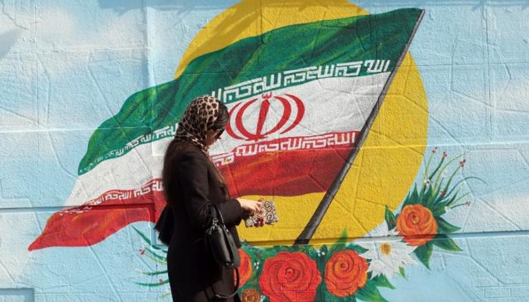 إيرانية تسير أمام جدارية علم 