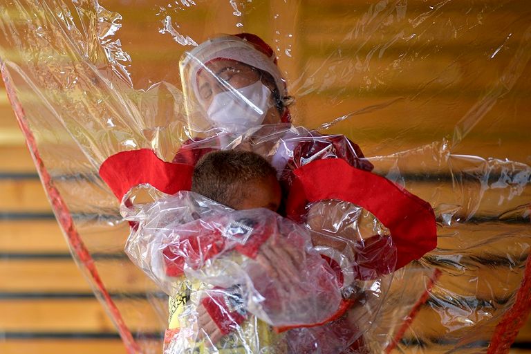 ماما نويل تقبل طفلة من وراء ستار بلاستيكي