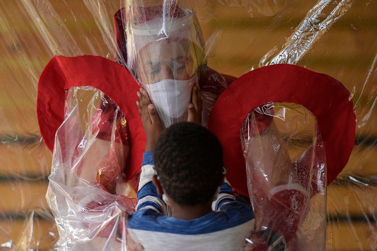 ماما نويل تقبل طفلة من وراء ستار بلاستيكي