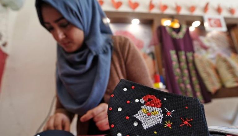 فتاة من غزة تعمل على كمامة ملونة لعيد الميلاد