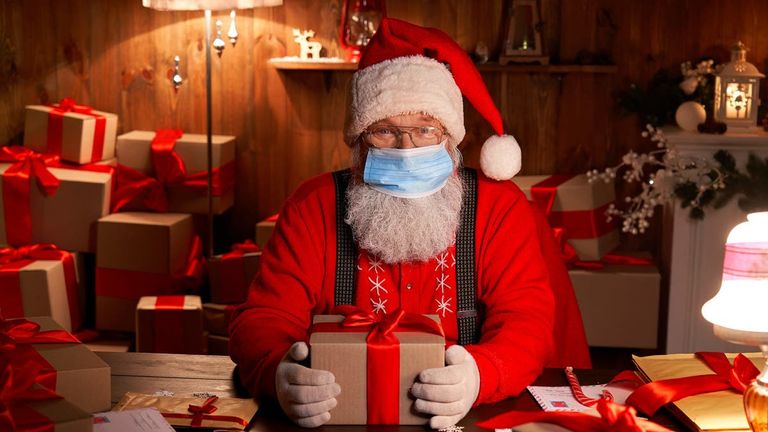 سانتا كلوز (بابا نويل) يرتدي الكمامة للوقاية من كورونا طفلان يتحدثان مع بابا نويل المحتمي بفقاعة