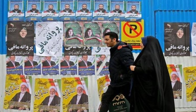 إيرانيون أمام ملصقات دعائية لمرشحي الانتخابات البرلمانية