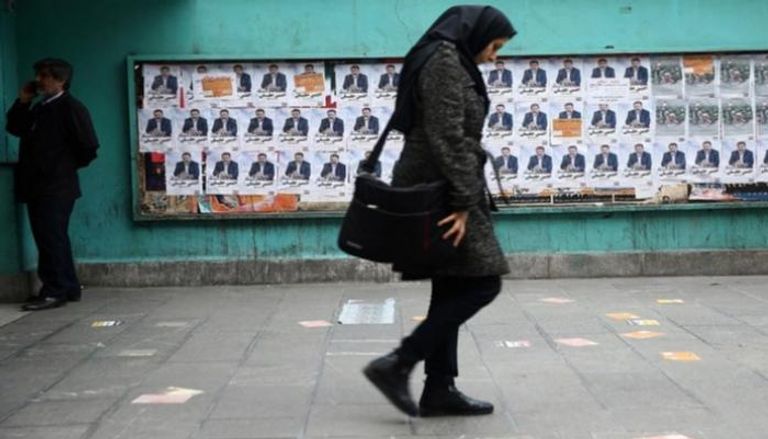 امرأة تمشي أمام دعاية انتخابية إيرانية - رويترز