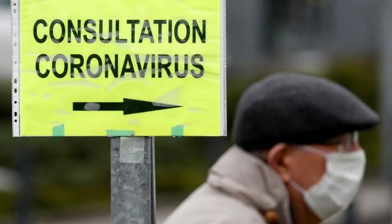 رجل يرتدي كمامة يسير بجوار لافتة تشير إلى مركز فحص لفيروس كورونا في فرنسا