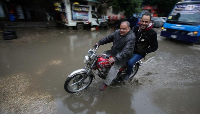 مصريان يركبان دراجة نارية خلال عاصفة رعدية وأمطار غزيرة في وسط القاهرة